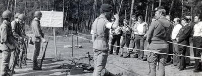 Soldaten in Uniform nehmen an einer militärischen Übung im Freien teil, während ein Offizier Anweisungen gibt.