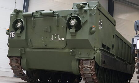Ein grüner Militärpanzer mit der Nummer 16 steht in einer Halle auf grauem Boden.