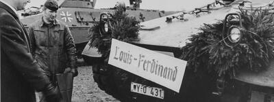 Ein gepanzerter Militärwagen mit dem Schild "Louis-Ferdinand" wird von zwei Männern inspiziert, darunter ein Soldat.