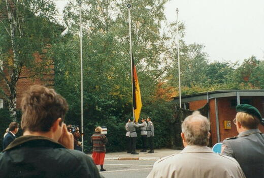 Menschen beobachten das Einholen der Dienstflagge vor der Bismarck-Kaserne im Jahr 1994.