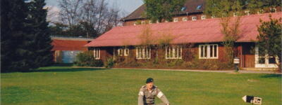 Ein Soldat sitzt neben Waffen und Munition auf dem Rasen vor einem Gebäude mit der Nummer 5 in der BBK.