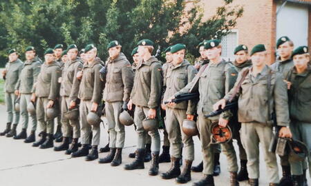 Eine Gruppe von Soldaten steht in Uniform und mit grünen Baretten aufgereiht für einen Wettkampf vor einem Backsteingebäude.