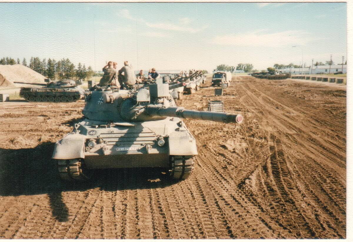 Eine Reihe von Panzern steht auf einem Übungsgelände, Soldaten sitzen auf dem vorderen Fahrzeug.