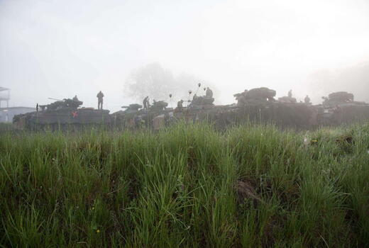 Panzer und Soldaten üben im morgendlichen Nebel hinter einer grünen Wiese während des Gefechtsbild-Trainings.