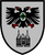 Ein Wappen zeigt einen schwarzen Doppeladler mit grünem Herzschild über einem stilisierten Gebäude auf grauem Hintergrund.