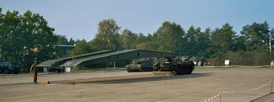 Ein Militärfahrzeug baut eine Brücke auf einem abgesperrten Platz vor einem Waldstück auf.