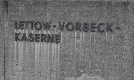 Ein Schild mit der Aufschrift "Lettow-Vorbeck-Kaserne" ist auf einer Betonwand angebracht.