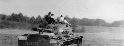 Ein Panzer fährt über ein Feld, während mehrere Personen auf ihm sitzen und die Landschaft genießen.
