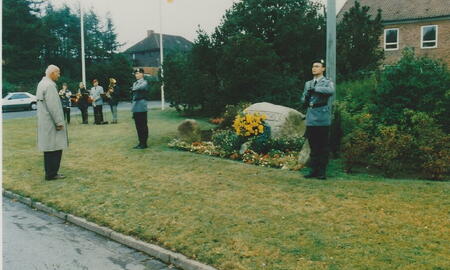 Ein Mann in Trenchcoat gedenkt am 9. September 1988 vor einem mit Blumen geschmückten Gedenkstein, flankiert von Soldaten.