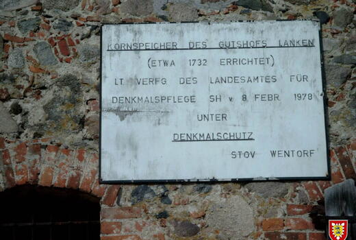 Ein Schild an einer alten Steinmauer informiert über den Denkmalschutz des Kornspeichers von 1732.