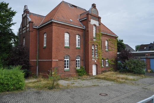 Ein altes Backsteingebäude der Eider Kaserne, von Efeu bewachsen, steht verlassen in einer überwucherten Umgebung.