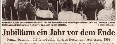 Eine Gruppe von Menschen sitzt bei einer feierlichen Ansprache im Freien, während zwei Porträtfotos oben rechts eingeblendet sind.