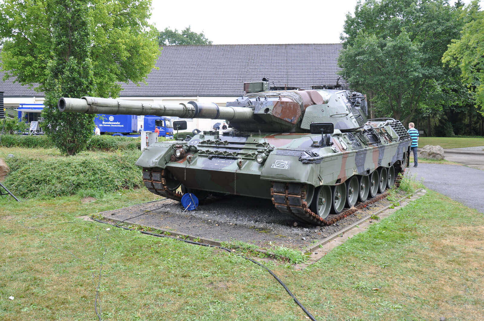Ein Leopard 1 Panzer steht auf einem Platz in Eutin, umgeben von Bäumen und einem Gebäude im Hintergrund.