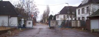 Ein leerer, asphaltierter Eingang zu einem alten Depot mit Gebäuden und kahlen Bäumen an einem bewölkten Tag.