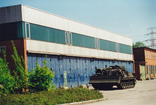 Ein Militärfahrzeug steht vor einer blauen Halle der Bismarck-Kaserne, umgeben von grüner Vegetation.