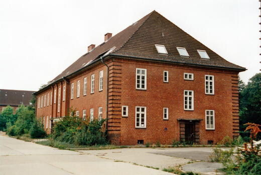 Ein rotes Backsteingebäude der Bismarck-Kaserne von 1996 steht von Pflanzen umgeben auf einem verlassenen Gelände.