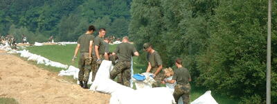 Soldaten errichten am 28. August 2002 eine Sandsackbarriere zur Hochwasserabwehr in einer grünen Landschaft.