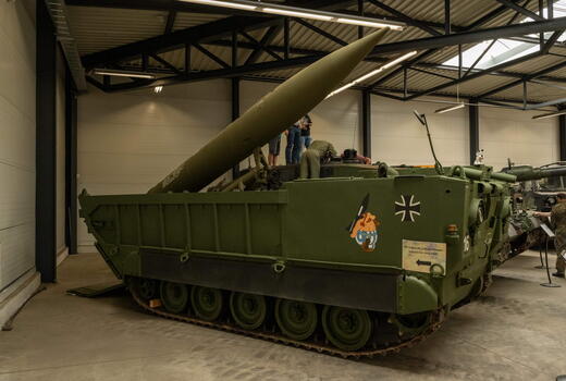 Ein grüner Militärpanzer mit Rakete wird in einem Museum ausgestellt, während Besucher ihn betrachten.