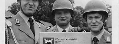Drei Soldaten der Panzerjägerkompanie 160 posieren in Uniform vor einem Schild in Elmenhorst.