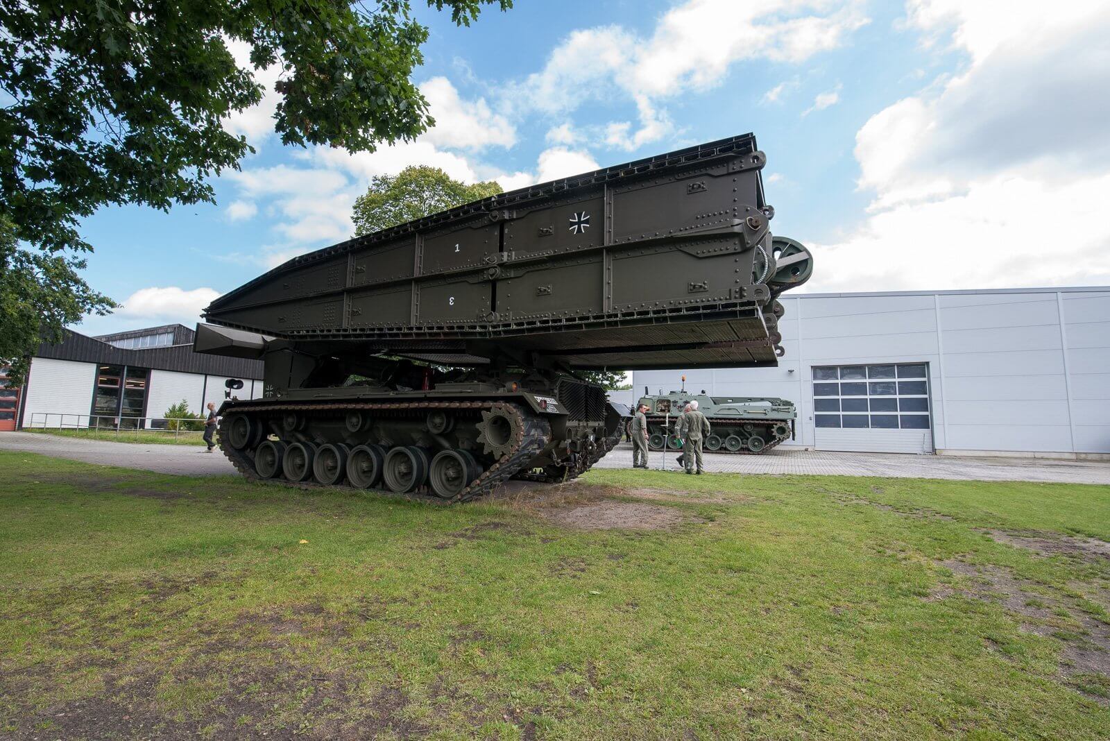 Ein Pionierpanzer mit Brücke wird bei einer Vorführung von Soldaten inspiziert.